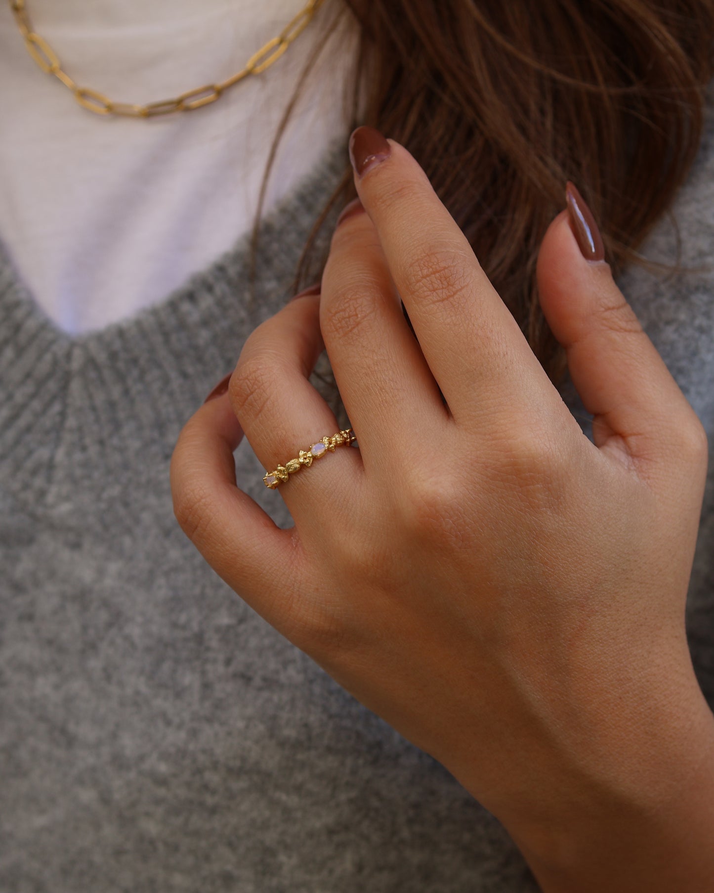 Close-up of a woman's hand wearing the gold Coral ring in 18k gold plated 925 sterling silver, styled with a grey sweater and a gold paperclip chain necklace.