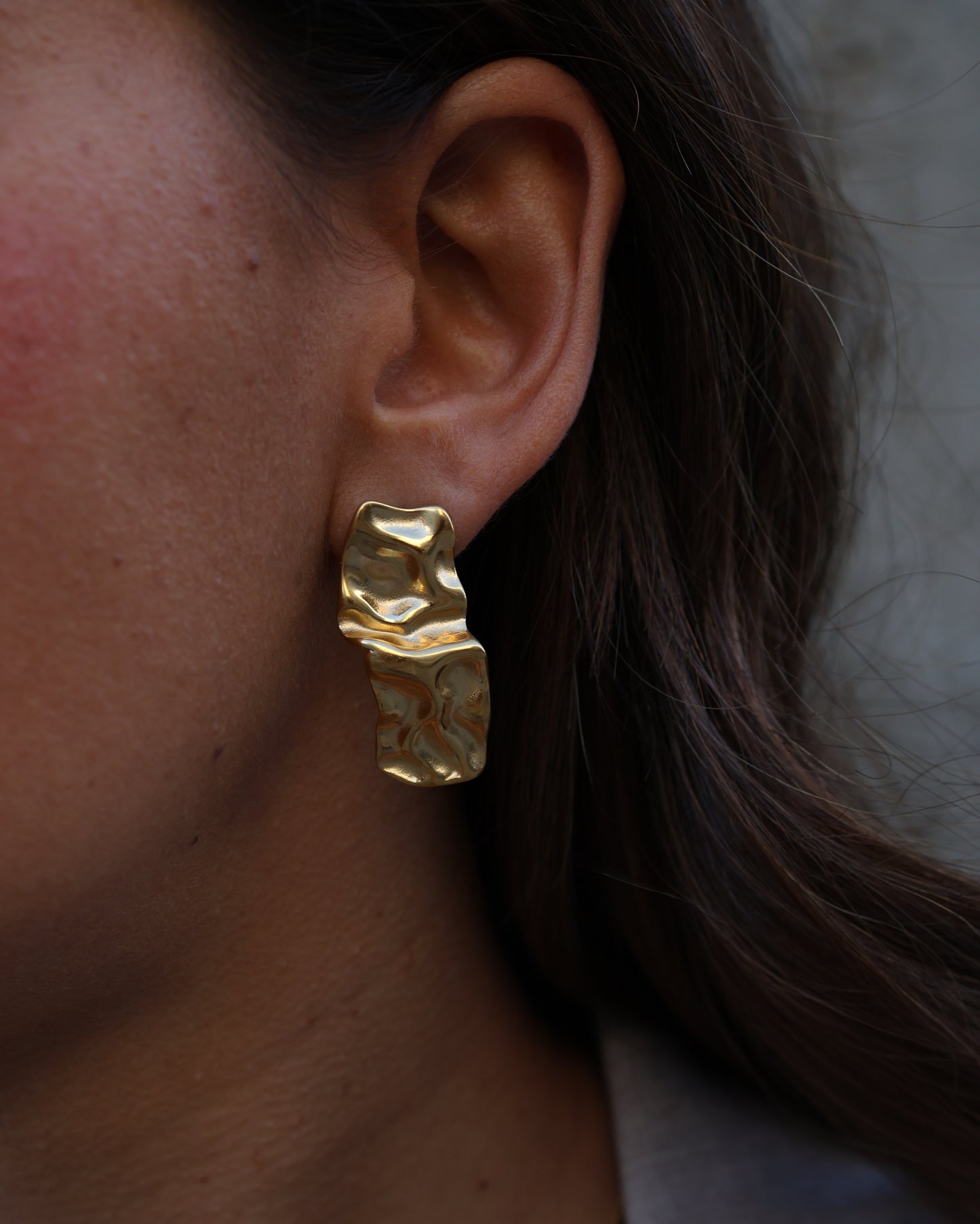 Extreme close-up of a gold Waves of Silence earring in 18k gold plated 316L stainless steel, highlighting the organic, liquid-metal rippled surface and high-shine finish.