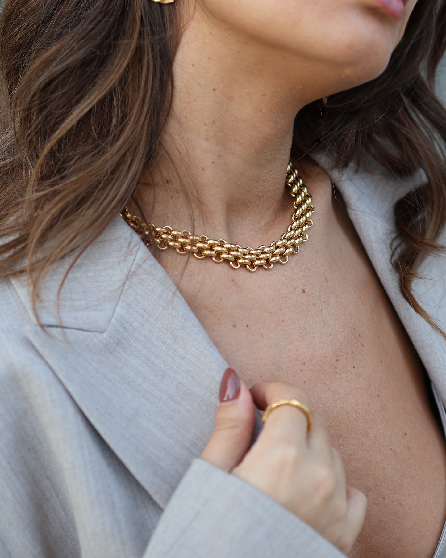 Close-up of the gold Nexus choker in 18k gold plated 316L stainless steel, styled with a grey tailored blazer and the gold Flow ring for a powerful, professional look.