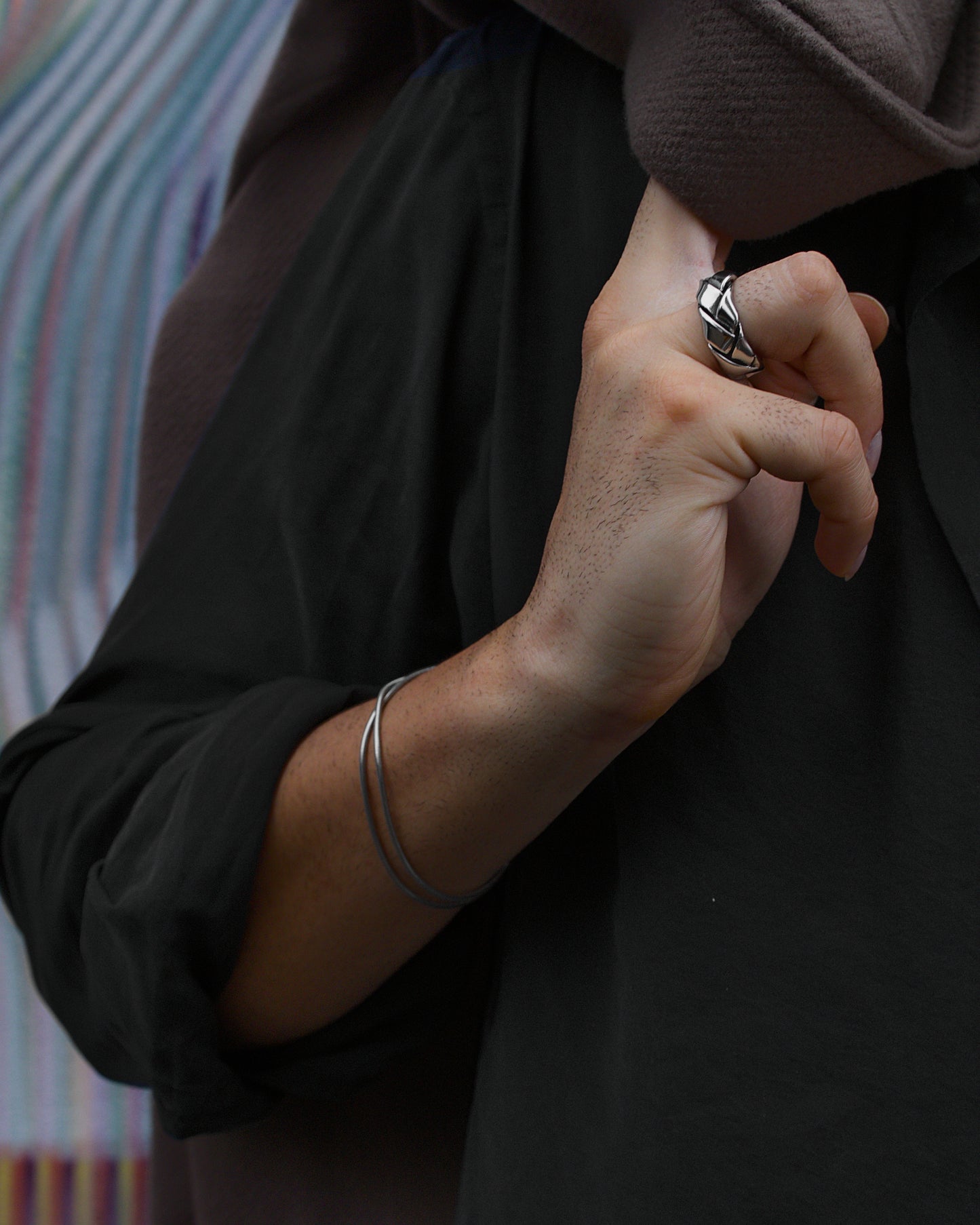 Man wearing two silver Serpentine bracelets and a wide silver Fracture ring, all crafted in polished 316L stainless steel.