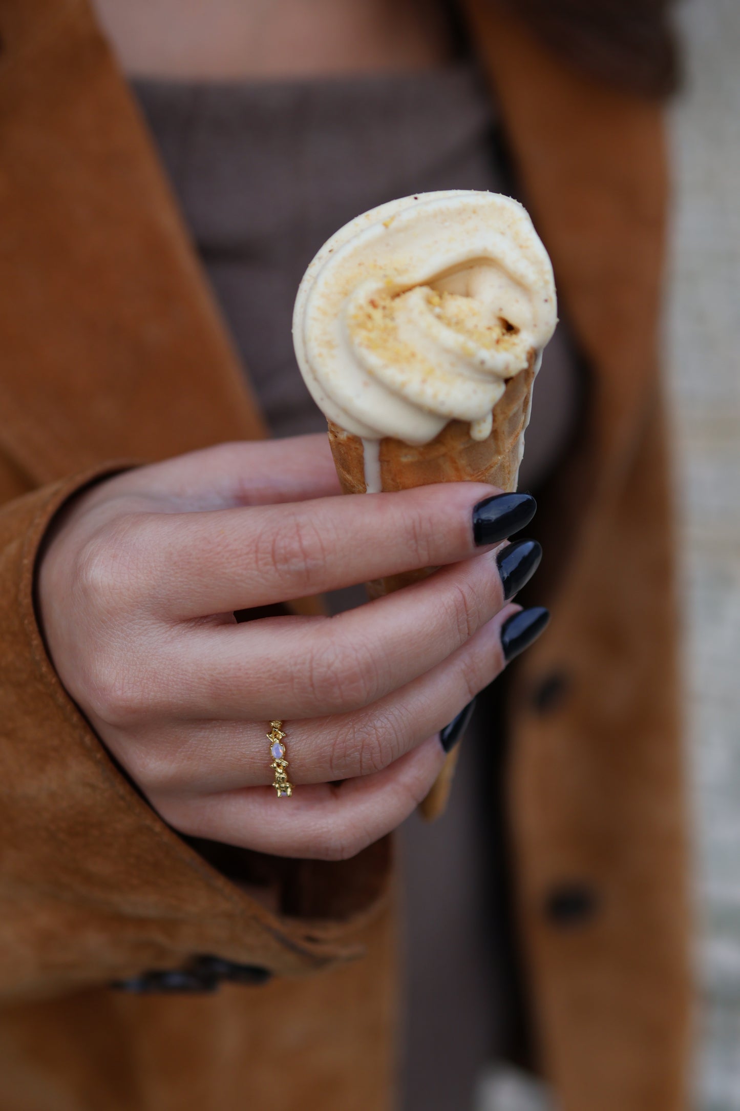 Close-up of a woman's hand with black nails holding an ice cream cone, wearing the gold Coral ring in 18k gold plated 925 sterling silver with opal details.