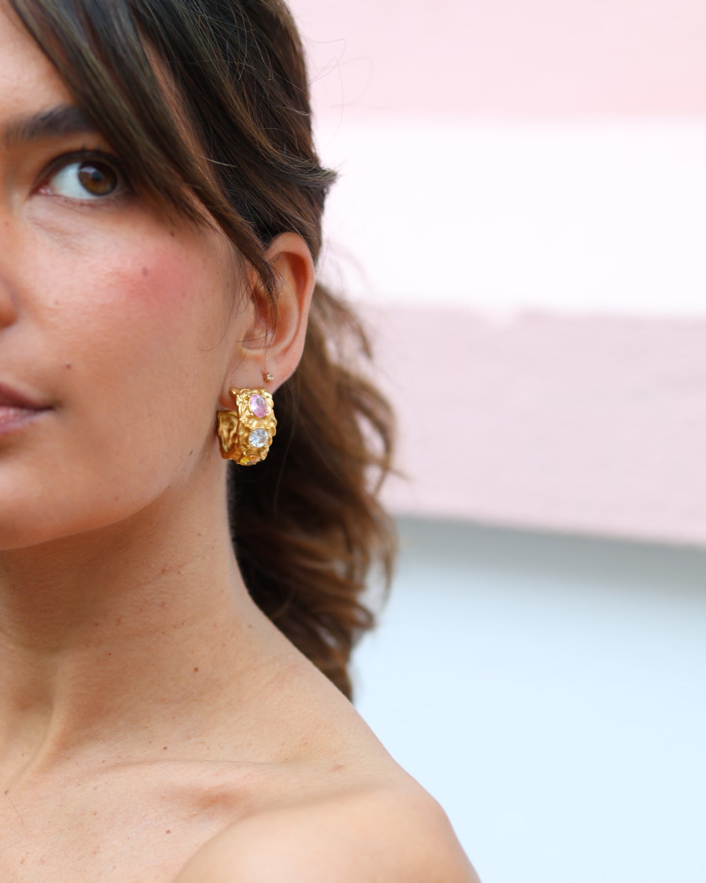 Woman wearing a single gold Crush hoop earring with pink and white crystal stones for a bold, contemporary look.