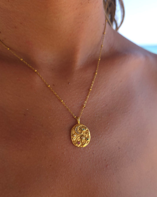Lifestyle close-up of the gold Celestial necklace in 18k gold plated 316L stainless steel, featuring its symbolic moon and star medallion against sun-kissed skin with a soft beach background.