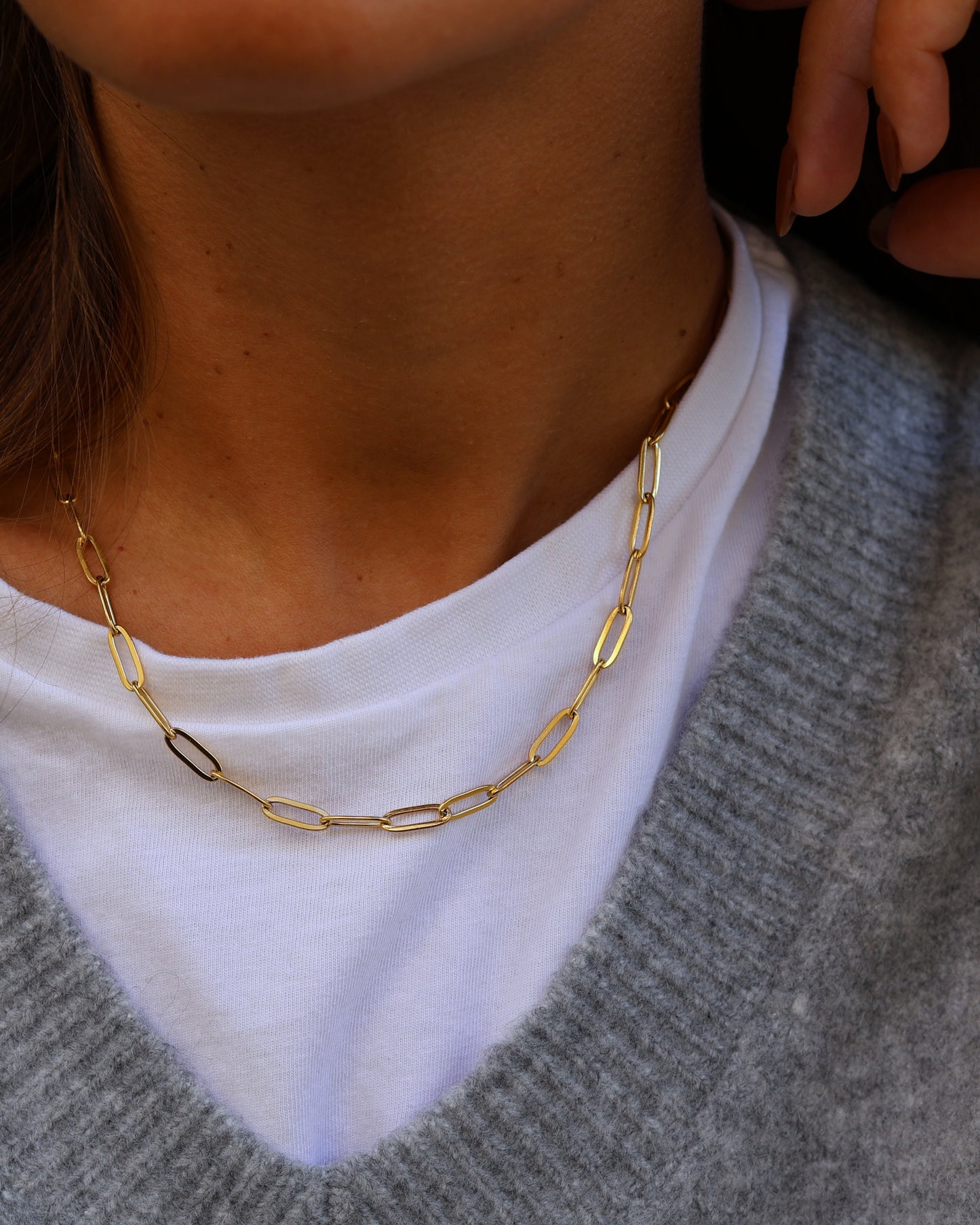 Close-up of the gold Echo chain necklace in 18k gold plated 316L stainless steel, featuring textured elongated links, styled over a white t-shirt and grey knit sweater.