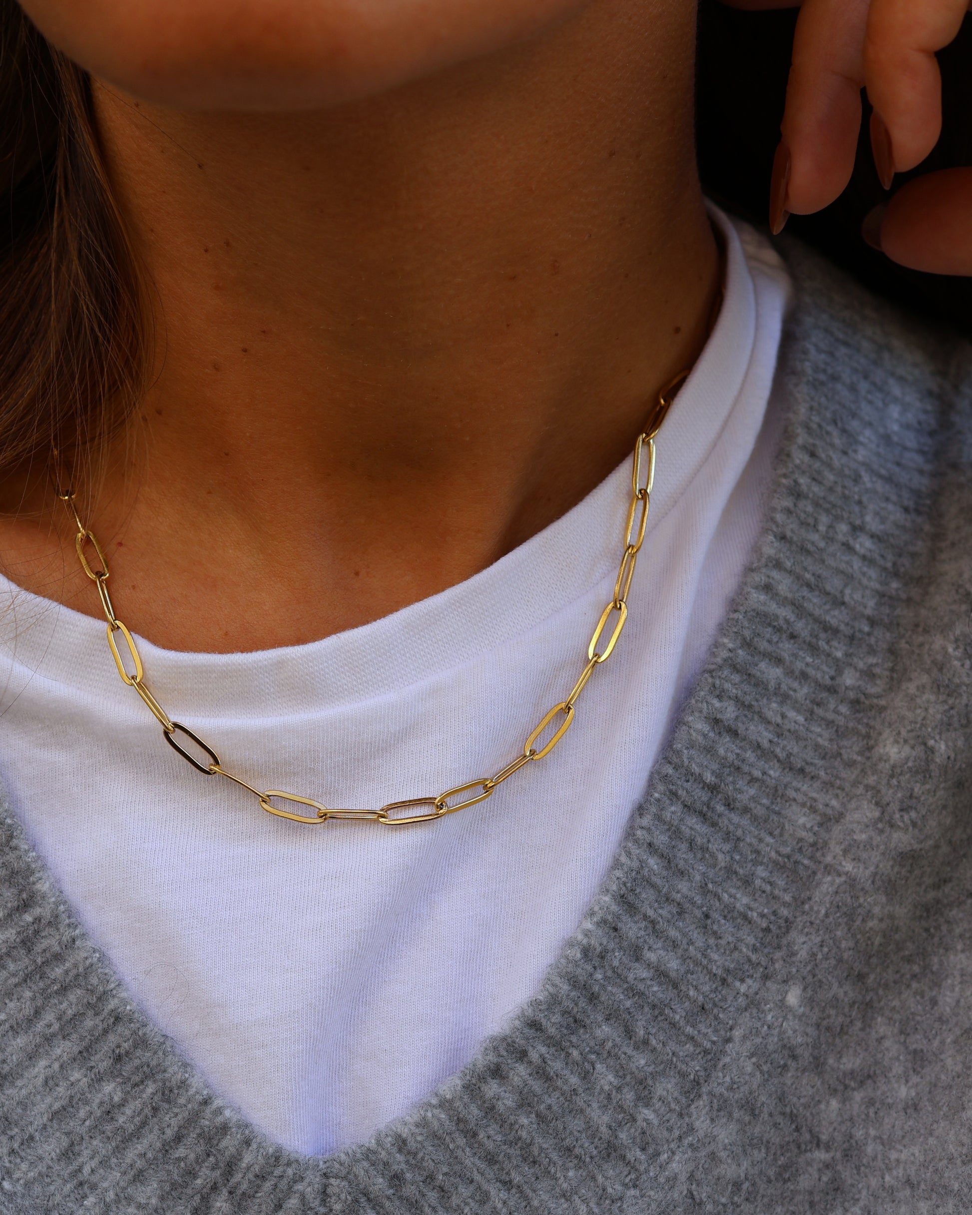 Close-up of the gold Echo chain necklace in 18k gold plated 316L stainless steel, featuring textured elongated links, styled over a white t-shirt and grey knit sweater.