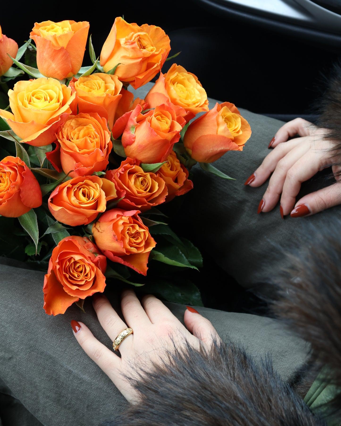 Woman wearing a textured gold astral ring sitting with a large bouquet of orange roses - SOMBRA Jewellery.