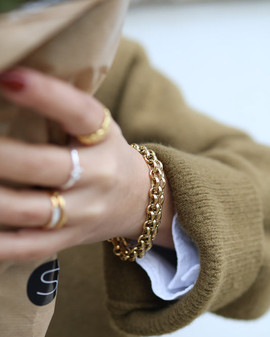 Close-up of a woman wearing the gold Nexus choker as a stacked bracelet with modern rings and olive knitwear.