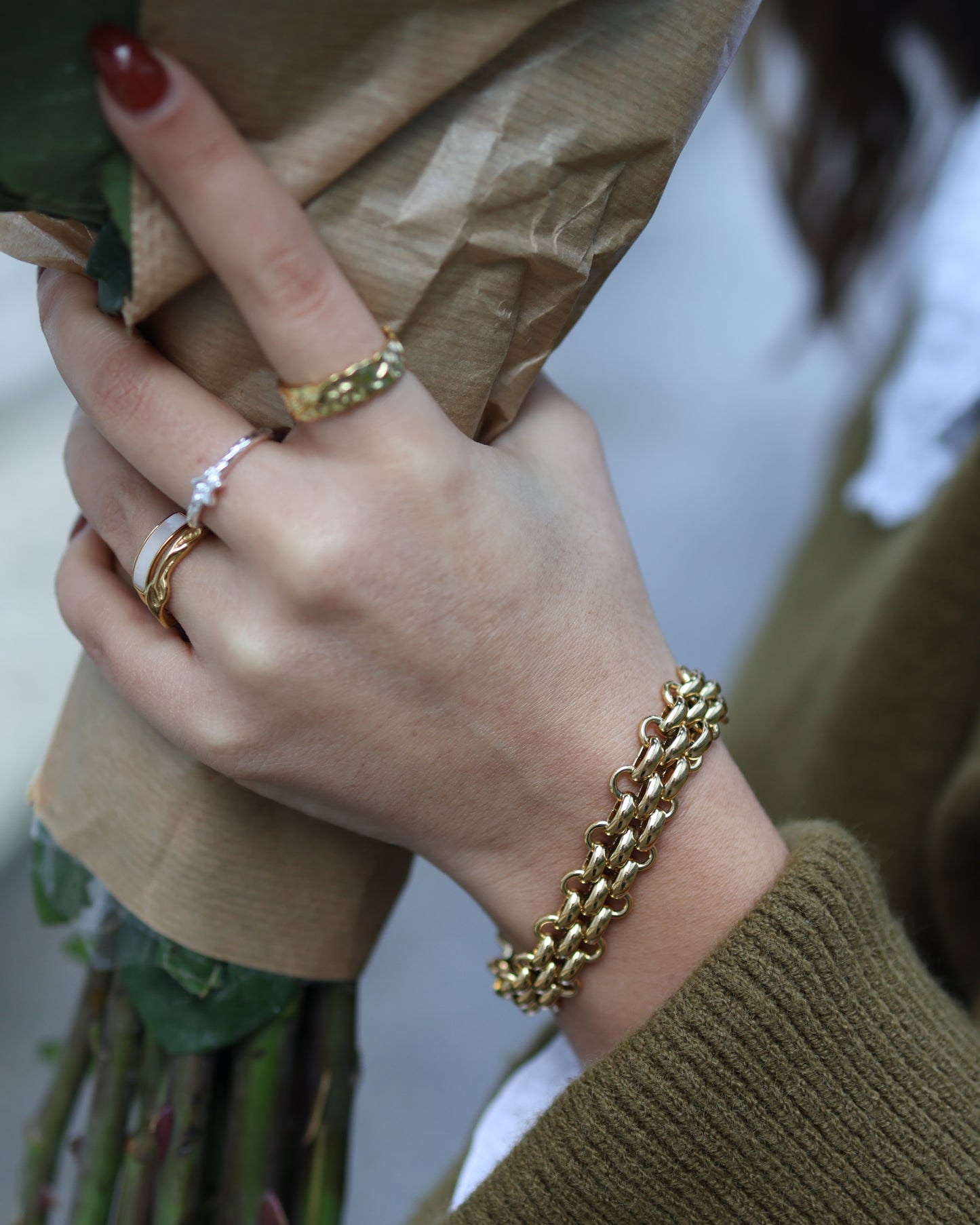 Person holding a bouquet of flowers wearing a chunky 18k gold plated chain bracelet and textured rings.
