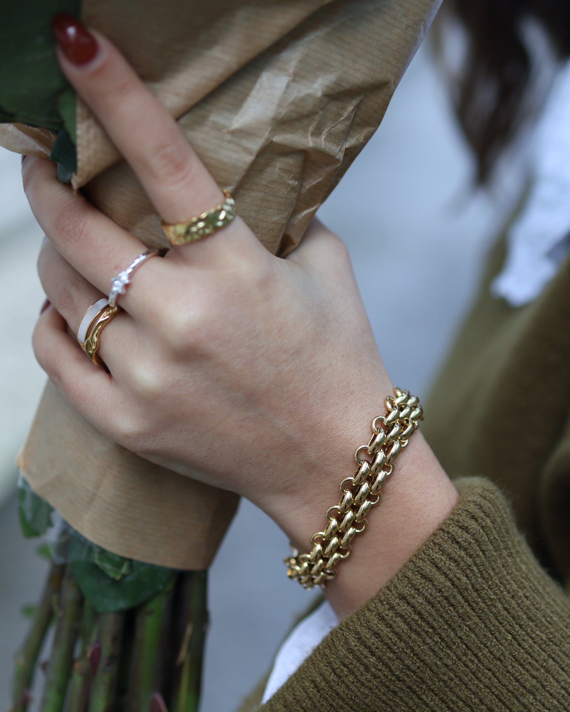Person holding a bouquet of flowers wearing a chunky 18k gold plated chain bracelet and textured rings.