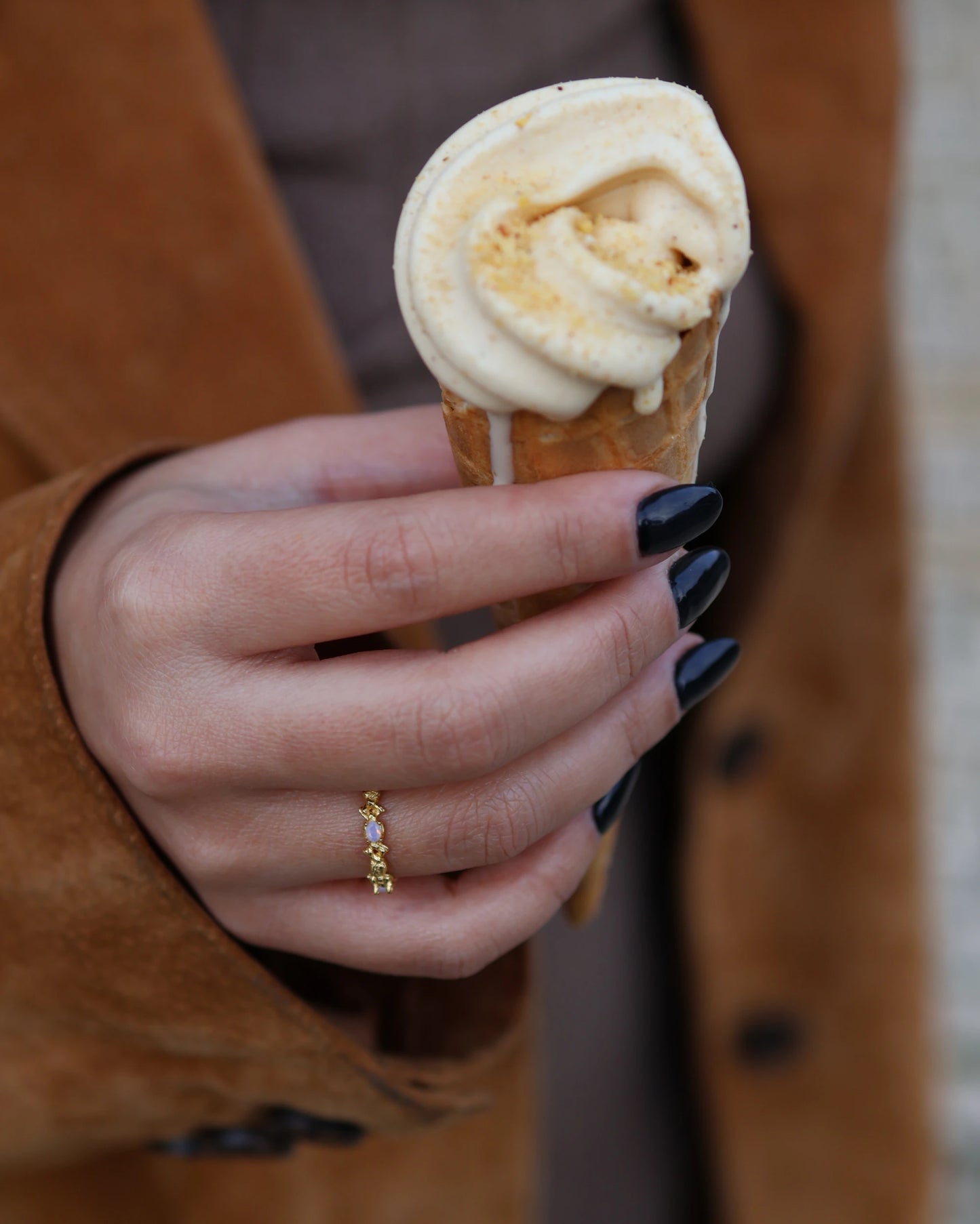 Close-up of a woman's hand with black nails holding an ice cream cone, wearing the gold Coral ring in 18k gold plated 925 sterling silver with opal details.